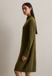 Grünes, gestricktes Kleid mit hohem Kragen, langen Ärmeln und gerippten Bündchen, im entspannten Schnitt und knielanger Länge.