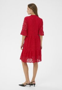 Rochie roșie din dantelă, cu tiv evazat, mâneci până la cot și talie ajustată, având modele florale și o textură netedă.