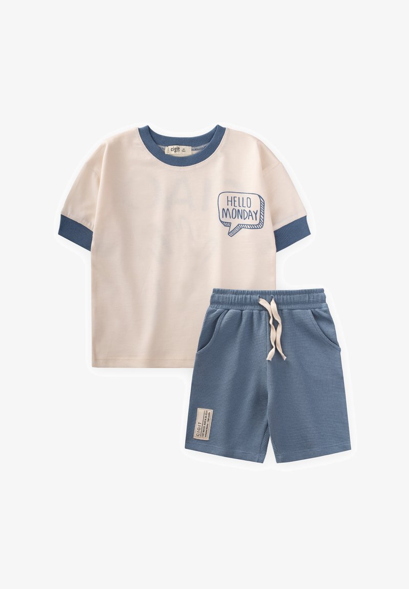 Pieno medvilnės marškinėliai trumpomis rankovėmis smėlio spalvos su mėlynais akcentais ir užrašu "SVEIKAS PIRMADIENI"; derinami su mėlynomis tekstūruotomis šortais su kišenėmis.