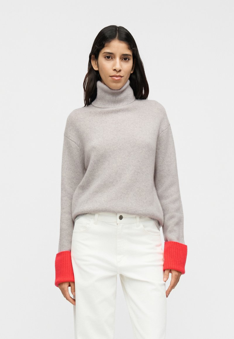 Ανοιχτό γκρι πουλόβερ με ζιβάγκο και ριμπ μανσέτες σε φωτεινό κόκκινο. Μαλακή υφή, oversized εφαρμογή, συνδυασμένο με άσπρο παντελόνι. Απλός και μοντέρνος σχεδιασμός.