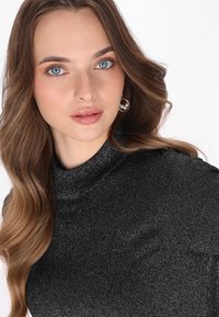 Sort, glitrende turtleneck top med en tætsiddende design. Modellen har langt, bølget hår og guld hoop øreringe med hvide perler.