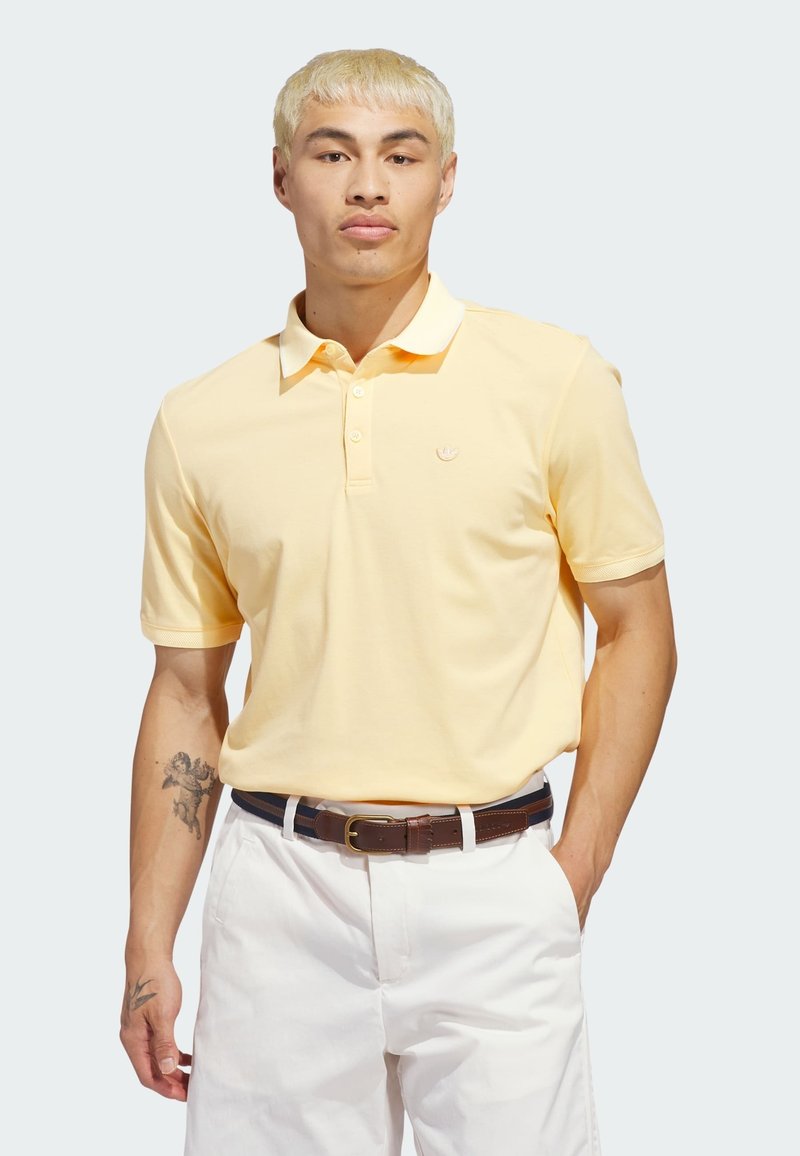 Πόλο μπλουζάκι σε παστέλ κίτρινο βαμβάκι, με γιακά, κοντά μανίκια, τρία κουμπιά και μικρό λογότυπο στο στήθος. Συνδυάζεται με λευκό παντελόνι.