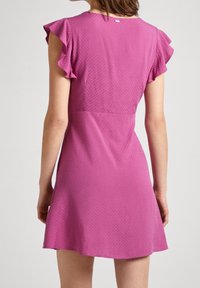 Rosa kort klänning med fjädrande ärmar, texturerad tyg, en åtsittande midja och utsvängd nederkant. Har ett subtilt mönster och detalj med baketikett.