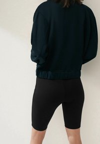 Felpa nera con una vestibilità rilassata e spalle cadenti, abbinata a pantaloni corti da ciclismo neri. Texture liscia, design minimale, senza motivi visibili.