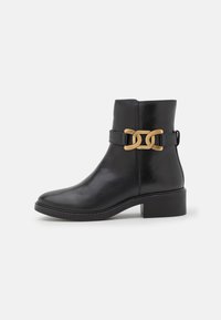 Bottines noires en cuir lisse avec un bout rond, dotées d'une élégante chaîne dorée autour de la cheville et d'un petit talon carré.