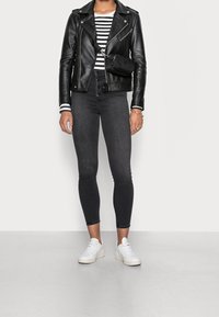 Chaqueta de cuero negra de motorista sobre una camiseta de rayas, combinada con jeans ajustados gris oscuro y zapatillas blancas. Incluye un pequeño bolso de hombro negro.