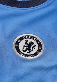 Tessuto azzurro chiaro con un logo ricamato rotondo del Chelsea Football Club. Presenta un leone nero su uno sfondo bianco, con dettagli beige.