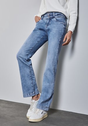 Jeans de denim azul claro con diseño de pierna recta, un leve desgastado y estilo de cinco bolsillos, combinados con zapatillas blancas.