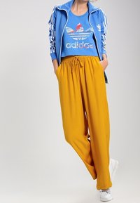 Starka gula, löst sittande byxor med elastiskt midjeband, tillsammans med en blå sweatshirt med en grafisk logotyp och randiga detaljer.