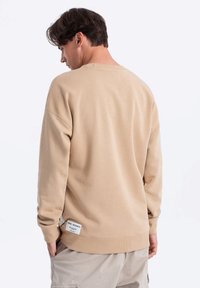 Beżowy sweatshirt o luźnym kroju, z prążkowanym okrągłym dekoltem i długimi rękawami. Posiada metkę na bocznym szwie. Gładka faktura.