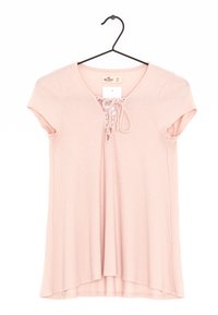 Růžový žebrovaný top s krátkými rukávy, výstřihem do V a šněrováním vpředu. Zavěšený na černém háčku.