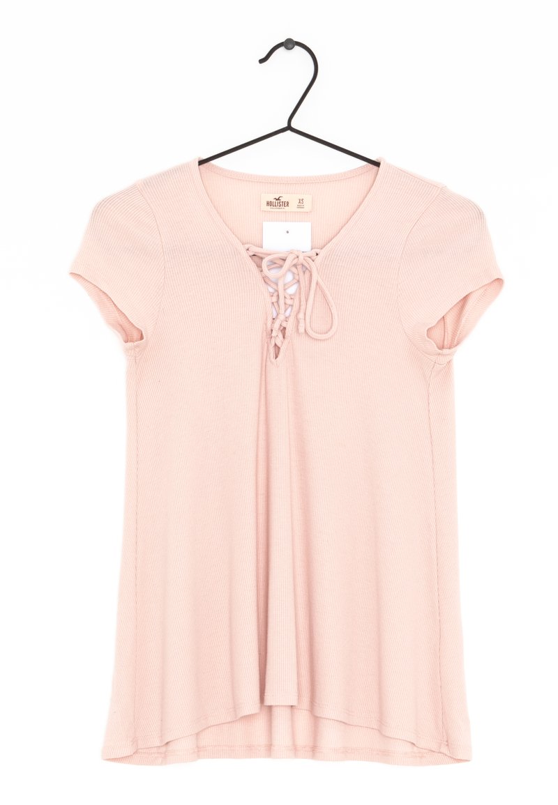 Růžový žebrovaný top s krátkými rukávy, výstřihem do V a šněrováním vpředu. Zavěšený na černém háčku.