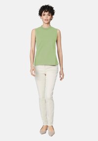 Lichtgroene mouwloze top met een hoge halslijn, gecombineerd met lichtgekleurde, getailleerde broek en platte schoenen. Gladde stof en klassieke snit.