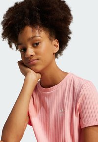 Rózsaszín bordázott póló kerek nyakkivágással, kis fehér Adidas logóval. Az anyag puha tapintású, rövid ujjú.