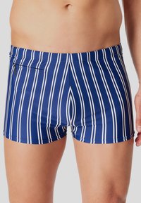 Modré plavkové kraťasy se svislými bíl�ými pruhy, slim fit střihem a malou kapsou na zip na zadní straně. Hladká textilie.