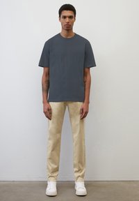 Szara bawełniana koszulka z okrągłym dekoltem, połączona z beżowymi spodniami o slim fit. Białe sneakersy dopełniają strój. Prosty design, minimalne akcenty.