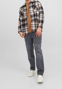 Camisa de franela a cuadros en azul marino, crema y óxido, llevada sobre una camiseta marrón; combinada con jeans grises y zapatillas blancas. Ajuste casual.