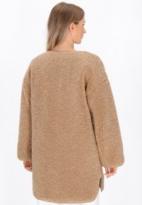 Giacca oversized in pile beige con un tessuto texturizzato e morbido. Presenta maniche lunghe e un orlo curvo, progettata per calore e comfort.