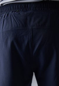 Pantaloni atletici de culoare albastru marin, cu un elastic în talie, având un buzunar cu fermoar și un material neted, ușor. Detalii cu cusătura pe spate.
