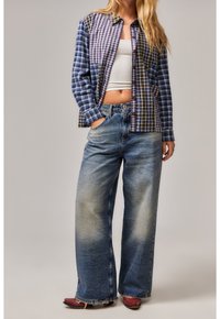 Ein Flanellhemd mit gemischten blauen und lila Karomustern, kombiniert mit weit geschnittenen, ausgewaschenen Denim-Jeans mit fransigen Kanten und hellerer Waschung.