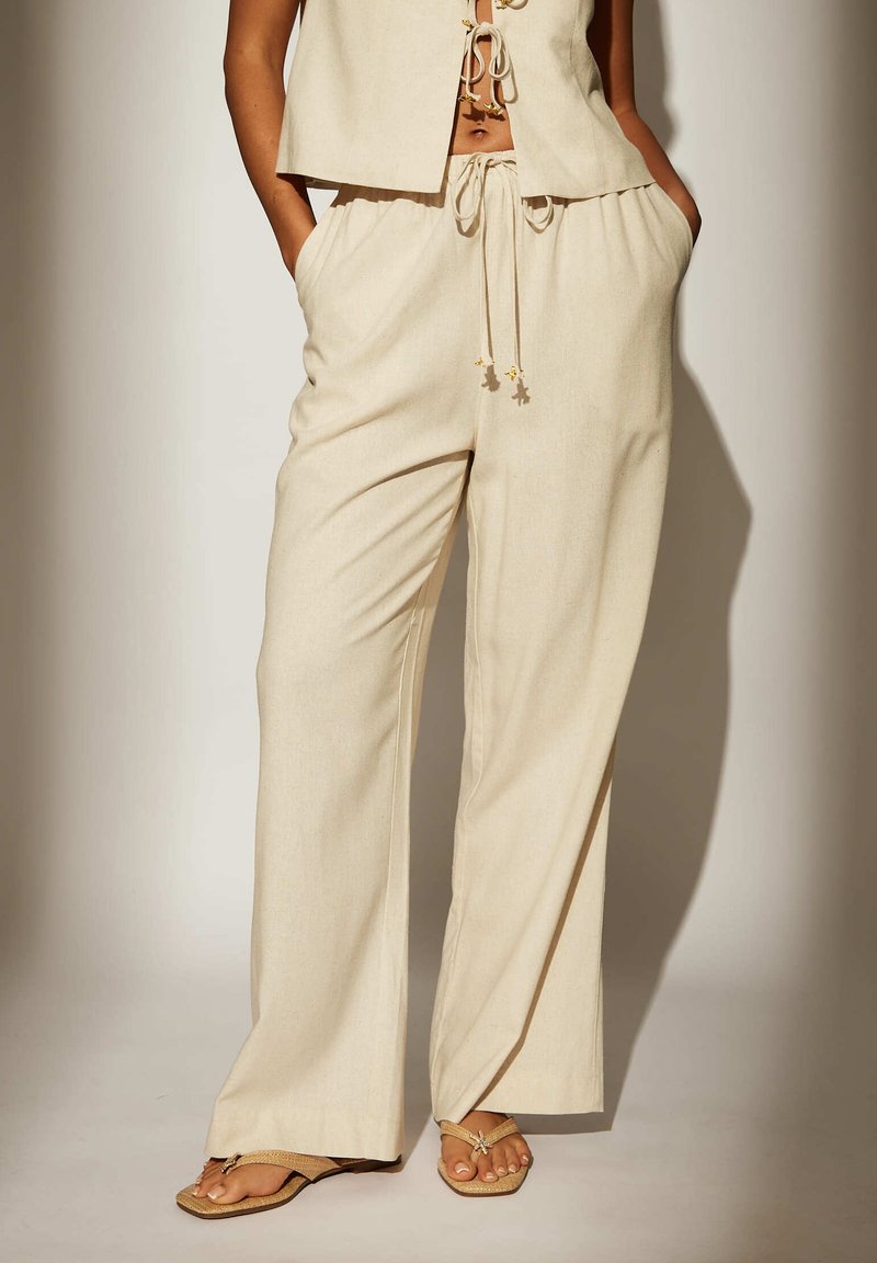 Pantalons larges beige en matériau léger, dotés d'une taille élastique avec des cordons de serrage et d'accents en étoile dorée.