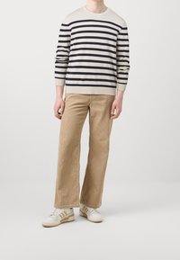 Maglione a righe lavorato a maglia in crema e blu navy, abbinato a pantaloni a gamba larga in corduroy beige e sneakers bianche con dettagli beige.