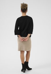 Črn pleten pulover s ¾ rokavi, bež krilo do kolen in črne gležnjarje. Gladka tekstura, preprost dizajn in prilega figura.