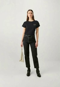 T-shirt de algodão preta com mangas curtas e decote redondo, apresentando um pequeno gráfico no peito. Combinado com jeans escuros de cintura alta e botas pretas.