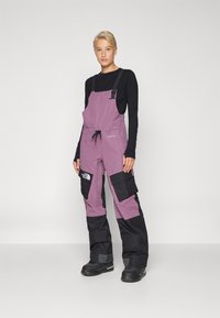 Lilla ja mustad lumeülikonnad, millel on reguleeritavad rihmad, elastne vöö ja mitmed suured taskud, valmistatud vastupidavast kangast. Sobivad külma ilma jaoks.