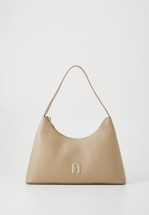 Sac à main beige avec un extérieur en cuir lisse, un design courbé et un accent en logo doré. Il dispose d'une bandoulière unique et d'une fermeture éclair.