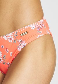 Bikini de parte inferior floral en tono rosa, con una cinturilla elástica, detalles de costura lateral y una pequeña etiqueta dorada con el logo "sunseeker".
