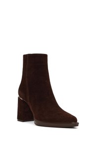 Bota de empeine marrón de ante con un tacón cuadrado grueso y punta puntiaguda. Presenta una textura suave y un diseño minimalista sin accesorios visibles.