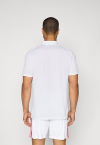 Hvid kortærmet skjorte med klassisk polo-design. Glat tekstur med en subtil krave. Et par hvide shorts med lyserøde sidelister.