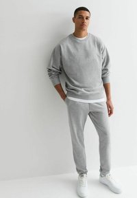 Sudadera de algodón gris con cuello redondo y puños elásticos, combinada con pantalones de chándal ajustados a juego y zapatillas blancas.