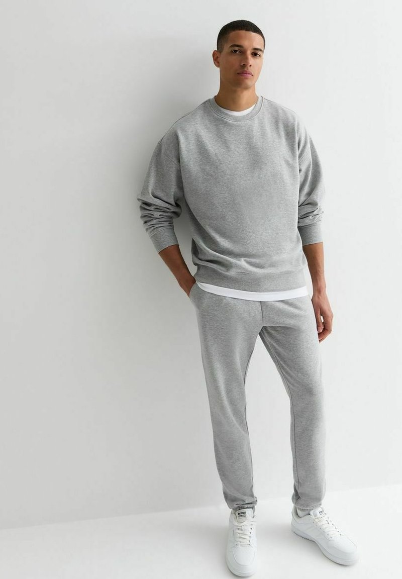 Sudadera de algodón gris con cuello redondo y puños elásticos, combinada con pantalones de chándal ajustados a juego y zapatillas blancas.