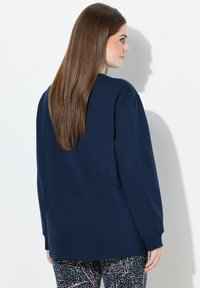 Camisa de manga larga azul marino hecha de una tela suave con un corte relajado; presenta un escote redondo y puños acanalados, combinada con pantalones estampados.