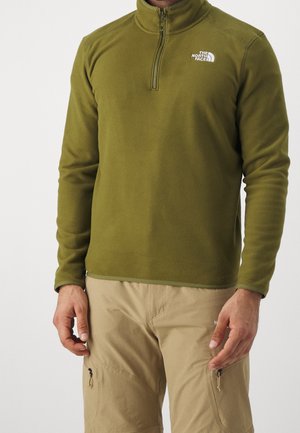 Forro polar de color verde oliva con cremallera hasta un cuarto, que presenta un cuello alto y un pequeño logo blanco en el pecho. Textura suave, diseño casual.