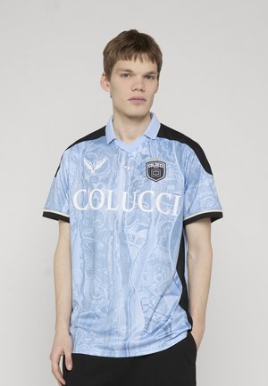Young man wearing a light blue Colucci short-sleeve jersey with black accents, standing against a plain white background.