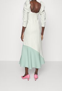 Robe à manches bouffantes en crème et menthe, avec un corsage ajusté et un ourlet évasé. Des chaussures à talons roses avec des accents ronds complètent le look.