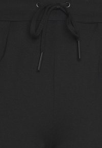 Calças de jogging pretas com um cós elástico e cordão, bolsos laterais e uma textura suave.