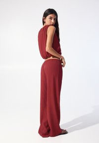 Röd, strukturerad tvådelad outfit bestående av en kort topp med lös passform och vida byxor. Enkel design utan synlig hårdvara eller mönster.