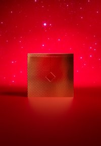 Packaging cuadrado rojo con superficie texturizada y detalle de patrón de diamante, contra un fondo rojo desenfocado con destellos.