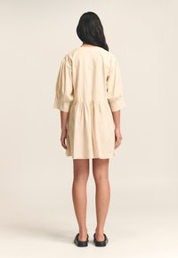 Beige katoenen jurk met een geplooide taille, pofmouwen en een ronde halslijn, met een ontspannen pasvorm en een lengte tot op de knie.