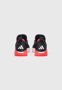Chaussures de sport noires avec semelles rouges, empeigne en maille et col rembourré. Présente un logo blanc et des accents rayés sur le talon.
