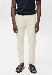 Pantaloni bej din bumbac, slim fit, cu buzunare standard. Asortați cu sandale negre din piele, cu bretele largi și catarame.