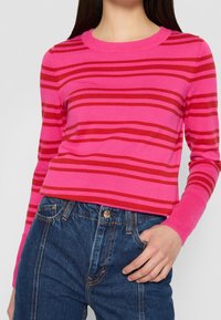 Maglione a righe rosa e rosse con colletto girocollo e maniche lunghe, abbinato a jeans a vita alta blu, con un bottone dorato.