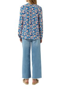 Blusa azul de estampado floral con mangas largas y pliegue en la espalda, combinada con vaqueros de pierna ancha en azul claro y sandalias de esparto.