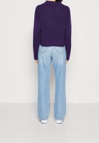 Lila korttröja med ribbad nederkant, tillsammans med ljusblå vida jeans. Outfiten inkluderar vita sneakers, sedd bakifrån.