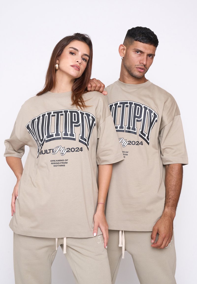 Las camisetas oversized beige presentan un atrevido texto negro con "MULTIPLICAR" y "2024" en el frontal. Combinadas con pantalones de chándal beige, de suave textura de algodón.