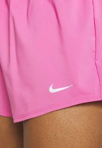 Vaaleanpunaiset urheilushortsit, jotka on valmistettu sileästä kankaasta, sisältävät valkoisen Nike-logon vasemmassa alareunassa, ja niissä on ommellut saumat sekä kevyt rakenne.